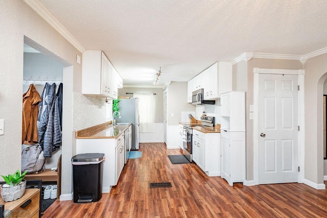 kitchen with appliances with stainless steel finishes, ornamental molding, a textured ceiling, dark wood-type flooring, and white cabinetry