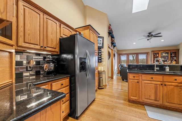 kitchen with dark stone counters, sink, light hardwood / wood-style flooring, ceiling fan, and stainless steel fridge