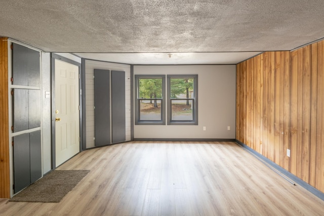 unfurnished room with a textured ceiling, light hardwood / wood-style floors, and wooden walls