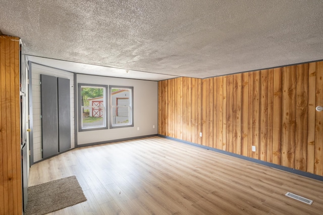 unfurnished room with a textured ceiling, light hardwood / wood-style floors, and wooden walls