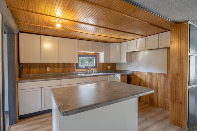 kitchen with white cabinets, sink, wooden walls, light hardwood / wood-style floors, and a kitchen island