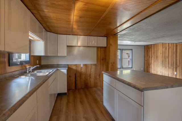 kitchen featuring white cabinets, light hardwood / wood-style flooring, wooden walls, and sink