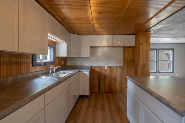 kitchen featuring light wood-type flooring, white cabinetry, wooden walls, and sink