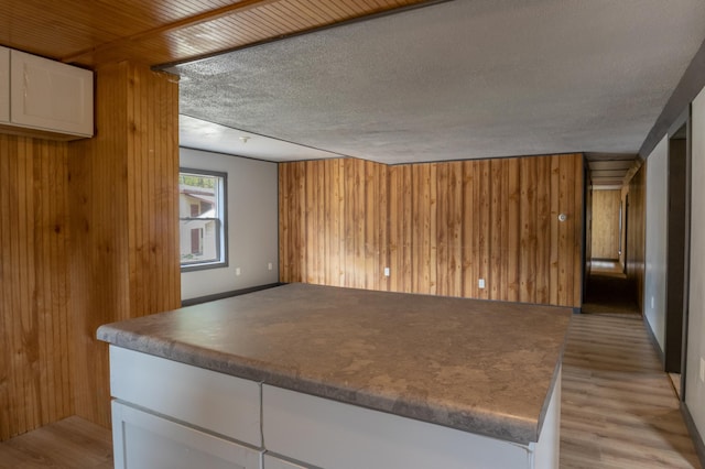 kitchen featuring white cabinets, light hardwood / wood-style floors, a textured ceiling, and wooden walls