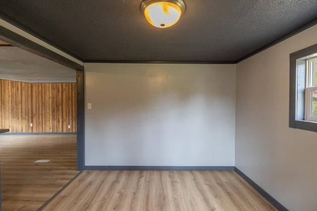 empty room featuring wood walls, light hardwood / wood-style flooring, a textured ceiling, and ornamental molding