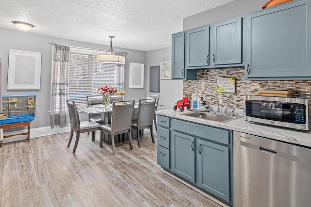 kitchen featuring sink, stainless steel appliances, light hardwood / wood-style flooring, blue cabinets, and pendant lighting