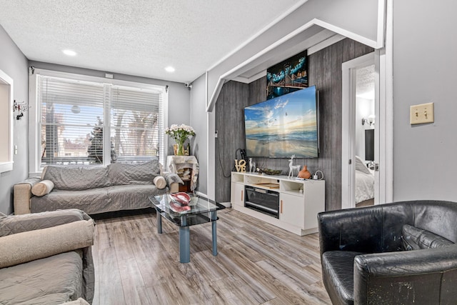 living room with wood walls, a textured ceiling, and light wood-type flooring