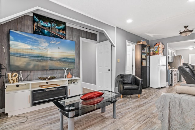 living room with a textured ceiling, light hardwood / wood-style floors, and wood walls