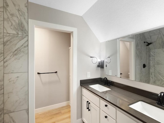 bathroom featuring wood-type flooring, a textured ceiling, lofted ceiling, tiled shower, and vanity