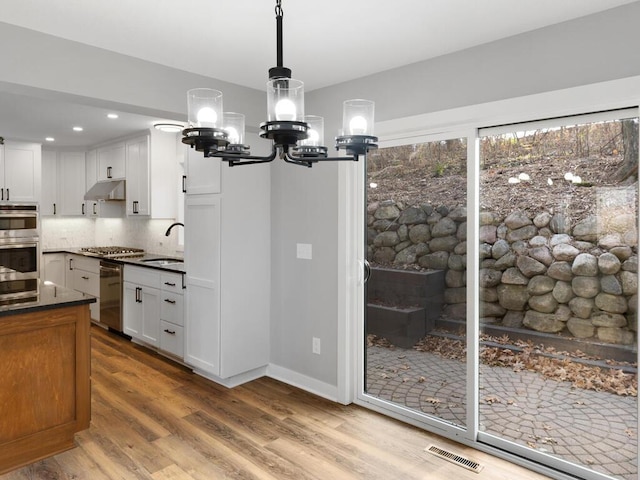 kitchen featuring backsplash, stainless steel appliances, sink, decorative light fixtures, and white cabinets