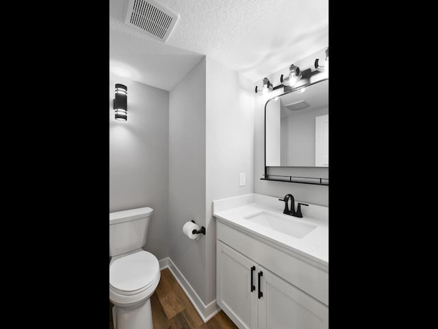 bathroom with hardwood / wood-style flooring, vanity, toilet, and a textured ceiling