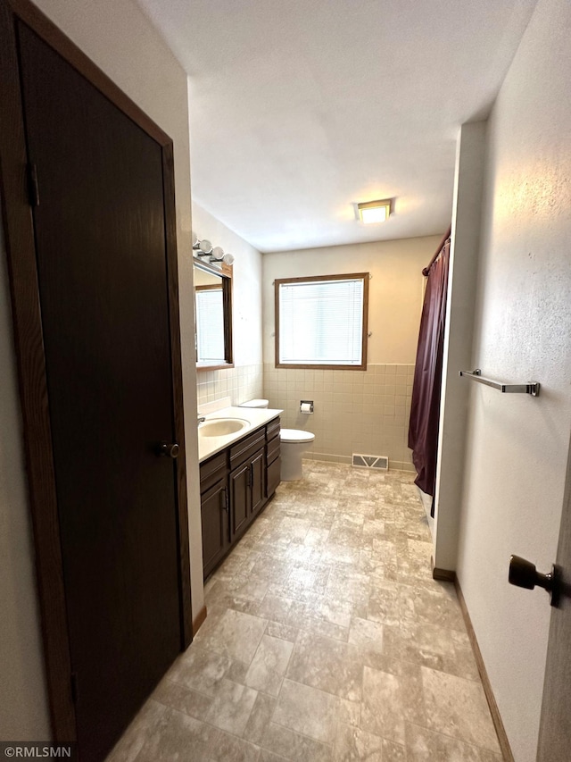 bathroom with vanity, toilet, and tile walls