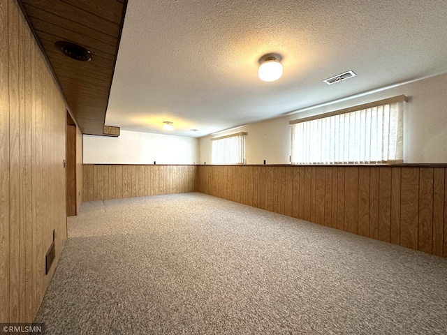 basement featuring carpet flooring, a textured ceiling, and wood walls