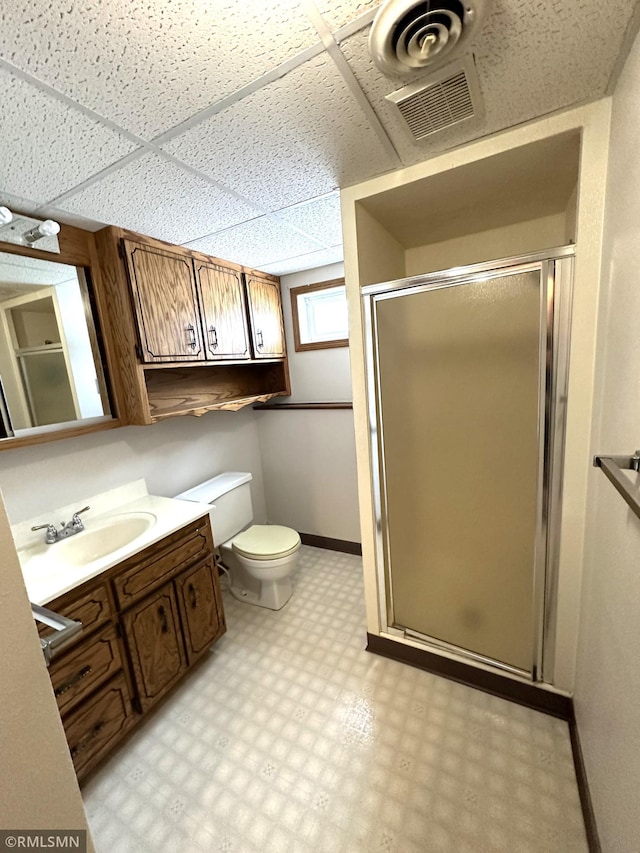 bathroom featuring a paneled ceiling, vanity, an enclosed shower, and toilet