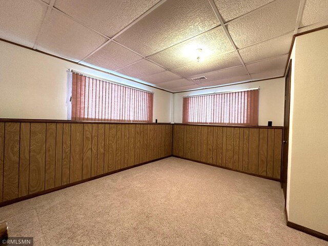 carpeted empty room featuring a paneled ceiling and wood walls