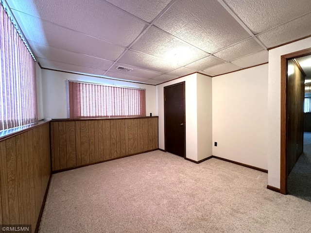 basement featuring a paneled ceiling, wood walls, and light carpet