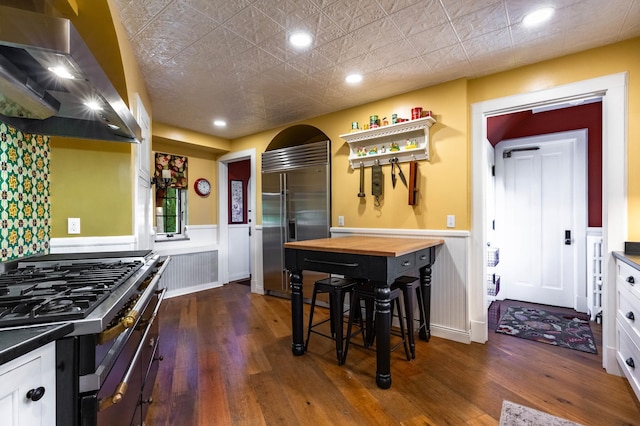 661 Market St, Winona, MN 55987 - kitchen featuring wooden counters, white cabinets, wall chimney exhaust hood, appliances with stainless steel finishes, and dark hardwood / wood-style flooring