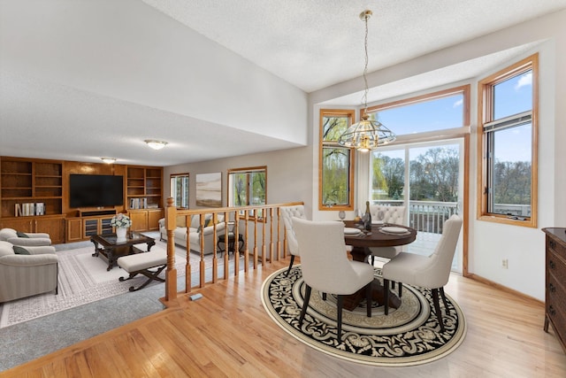 dining room featuring light wood-type flooring, a textured ceiling, baseboards, and a notable chandelier