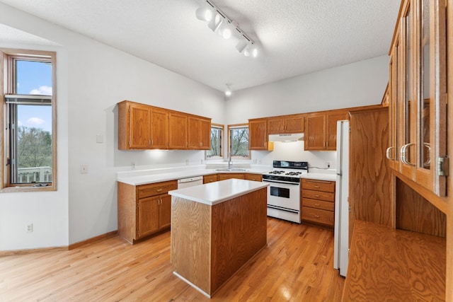 kitchen with brown cabinetry, a sink, light countertops, track lighting, and white appliances
