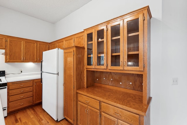 kitchen featuring white appliances, brown cabinetry, glass insert cabinets, and light wood-type flooring