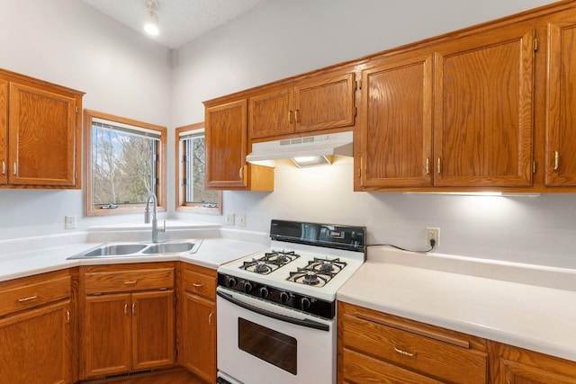 kitchen featuring white gas range, brown cabinetry, light countertops, a sink, and under cabinet range hood