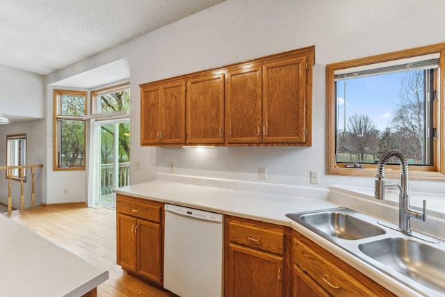 kitchen with light wood-style floors, light countertops, brown cabinets, a sink, and dishwasher