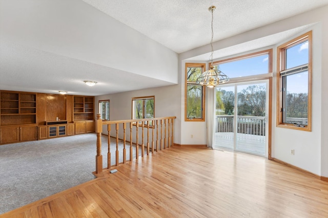 unfurnished dining area with an inviting chandelier, baseboards, a textured ceiling, and wood finished floors