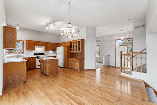 kitchen with brown cabinets, a notable chandelier, a sink, white appliances, and a center island