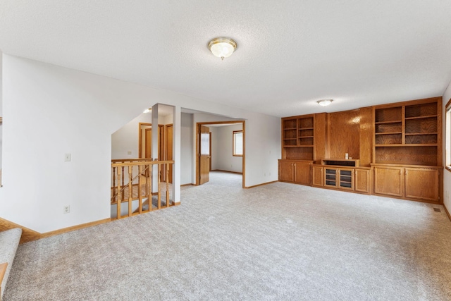 unfurnished living room with built in shelves, baseboards, a textured ceiling, and light colored carpet