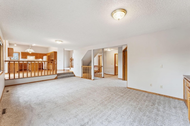 unfurnished living room featuring light colored carpet, a textured ceiling, stairs, and visible vents