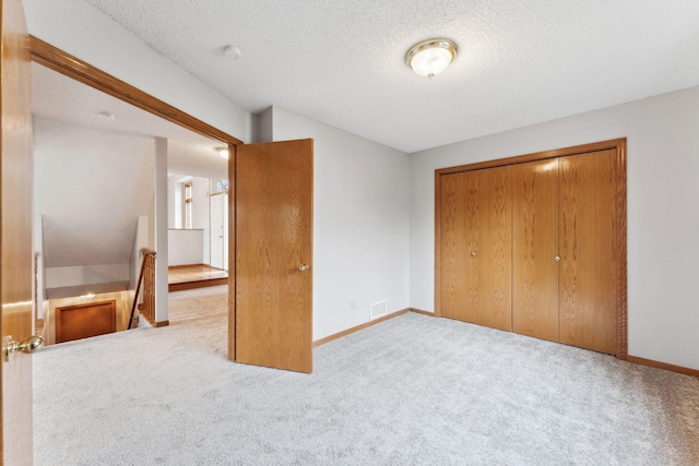 unfurnished bedroom with carpet floors, visible vents, a closet, baseboards, and a textured ceiling