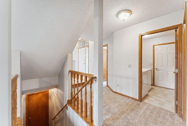 hallway with washer and dryer, light colored carpet, a textured ceiling, baseboards, and an upstairs landing