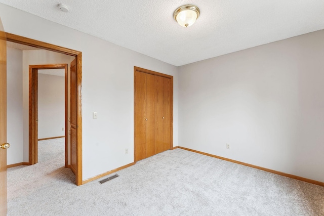 unfurnished bedroom featuring carpet floors, a textured ceiling, baseboards, visible vents, and a closet