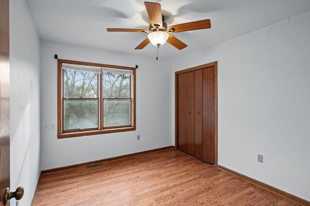 unfurnished bedroom with a textured ceiling, light hardwood / wood-style flooring, a closet, and ceiling fan