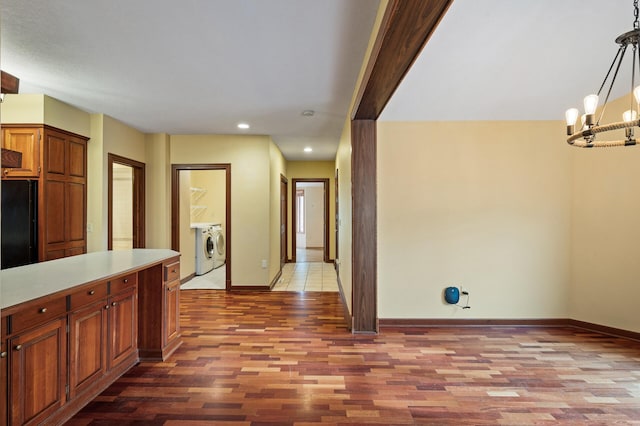 kitchen with hanging light fixtures, black refrigerator, a notable chandelier, washer and clothes dryer, and hardwood / wood-style floors