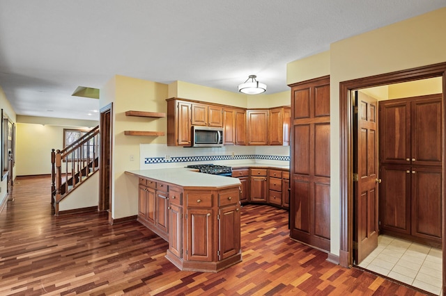 kitchen featuring tasteful backsplash, range, kitchen peninsula, and dark wood-type flooring