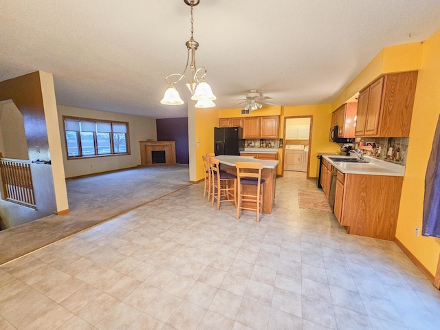 kitchen featuring a breakfast bar, hanging light fixtures, black appliances, a kitchen island, and washer / dryer