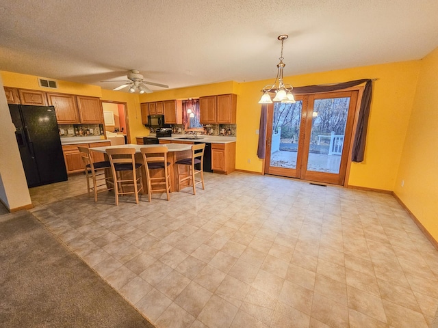 kitchen with a kitchen island, sink, a breakfast bar area, hanging light fixtures, and black appliances