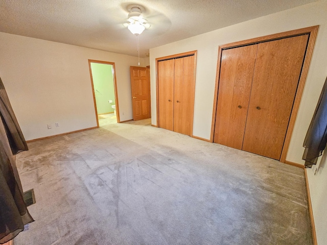 unfurnished bedroom featuring multiple closets, ensuite bathroom, light colored carpet, and a textured ceiling