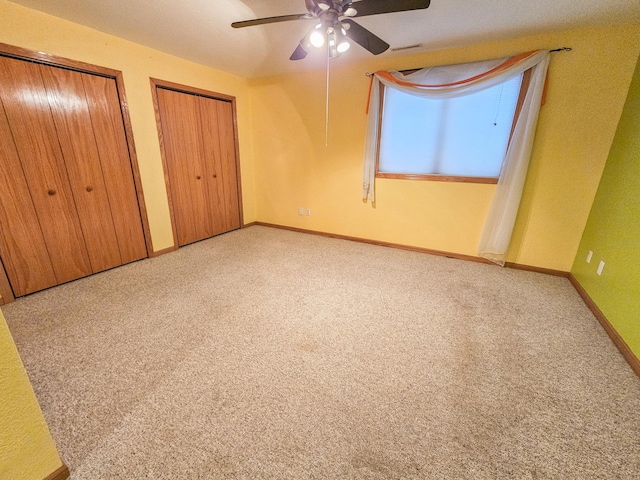 unfurnished bedroom with multiple closets, light colored carpet, and ceiling fan