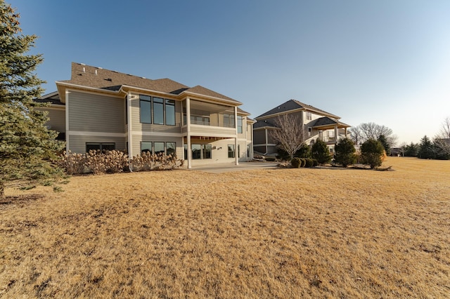 back of house featuring roof with shingles, a balcony, a yard, and a patio