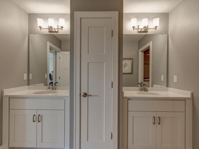 bathroom featuring a textured ceiling, a sink, and two vanities