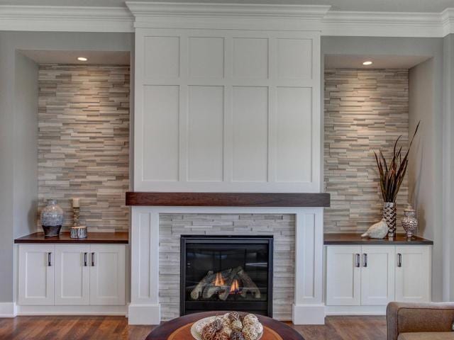 unfurnished living room featuring crown molding, dark wood-type flooring, and a glass covered fireplace