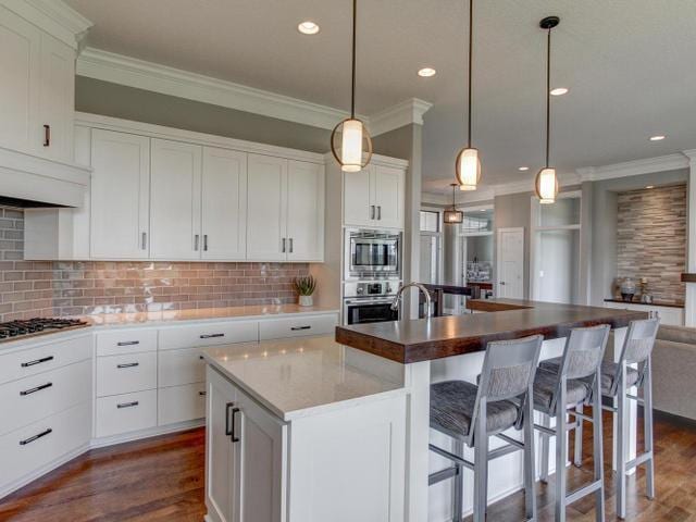 kitchen with ornamental molding, backsplash, a center island with sink, dark wood-style floors, and appliances with stainless steel finishes