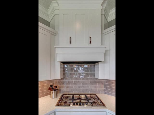 kitchen featuring stainless steel gas cooktop, tasteful backsplash, glass insert cabinets, custom range hood, and white cabinets