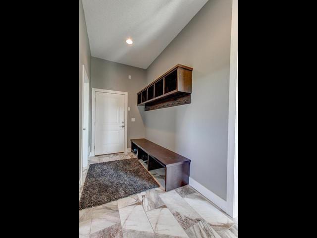 mudroom featuring marble finish floor, baseboards, and vaulted ceiling
