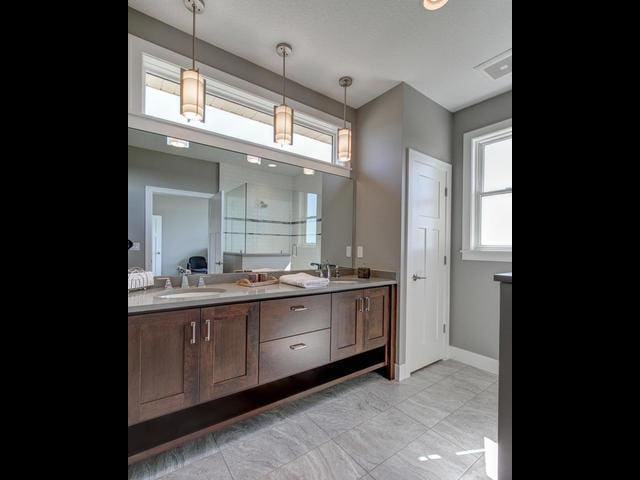 bathroom with double vanity, a sink, baseboards, and a shower with shower door