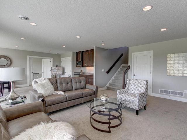 living area featuring light carpet, baseboards, visible vents, and stairway