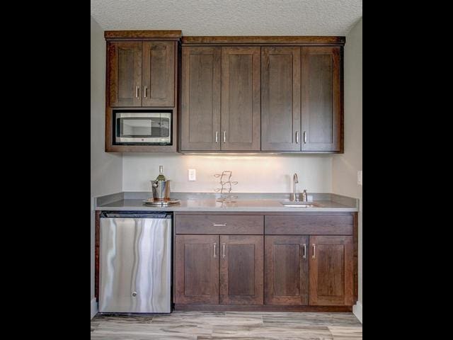 kitchen with light countertops, a textured ceiling, a sink, light wood-style floors, and appliances with stainless steel finishes