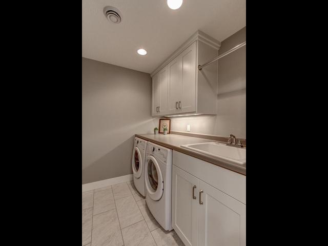 laundry room with light tile patterned floors, separate washer and dryer, a sink, visible vents, and cabinet space